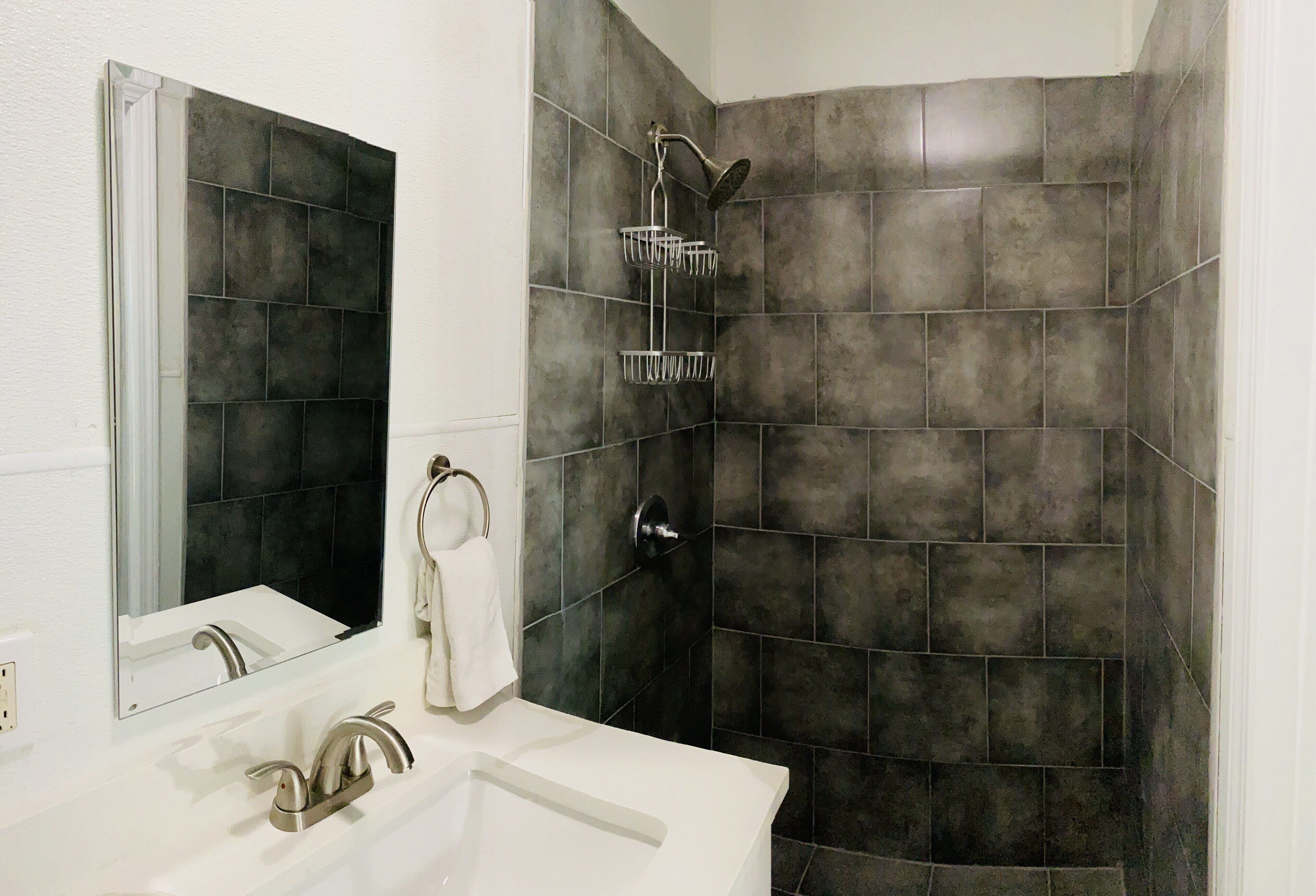A bathroom with a white sink, a mirror, and a shower with a dark tiled wall.