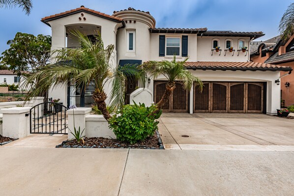 A two-story house with a garage, palm trees, and a concrete driveway.