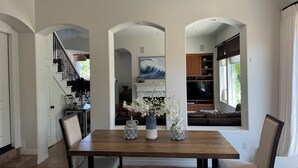 A dining area with a wooden table and chairs, a vase with flowers, and a view of a kitchen and living area through an archway. - Carlsbad Beach Resort- Across Street from Crystal Blue Beaches. (Carlsbad)