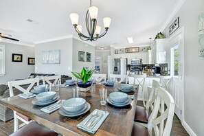 A dining area with a wooden table set for six, white chairs, and a chandelier.