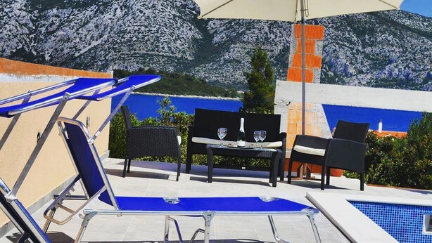 Ein Poolbereich mit Liegestühlen, einem Tisch mit Gläsern und einem großen Sonnenschirm.