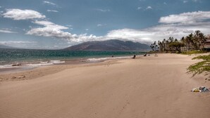Ein weiter Sandstrand mit freiem Blick auf den Ozean und einem Berg in der Ferne.