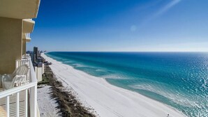 Uitzicht op het strand vanaf een balkon, met een heldere lucht, zandstrand en de oceaan.
