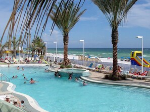 Ein Poolbereich mit mehreren Schwimmbecken, Palmen, Liegestühlen und einer Wasserrutsche.