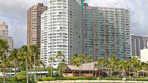 Ein Hochhaus-Hotel mit mehreren Balkonen, ein Strand im Vordergrund und Palmen.