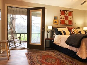 Une chambre avec un grand lit, un fauteuil à bascule, une porte donnant sur un balcon et un tapis à motifs.