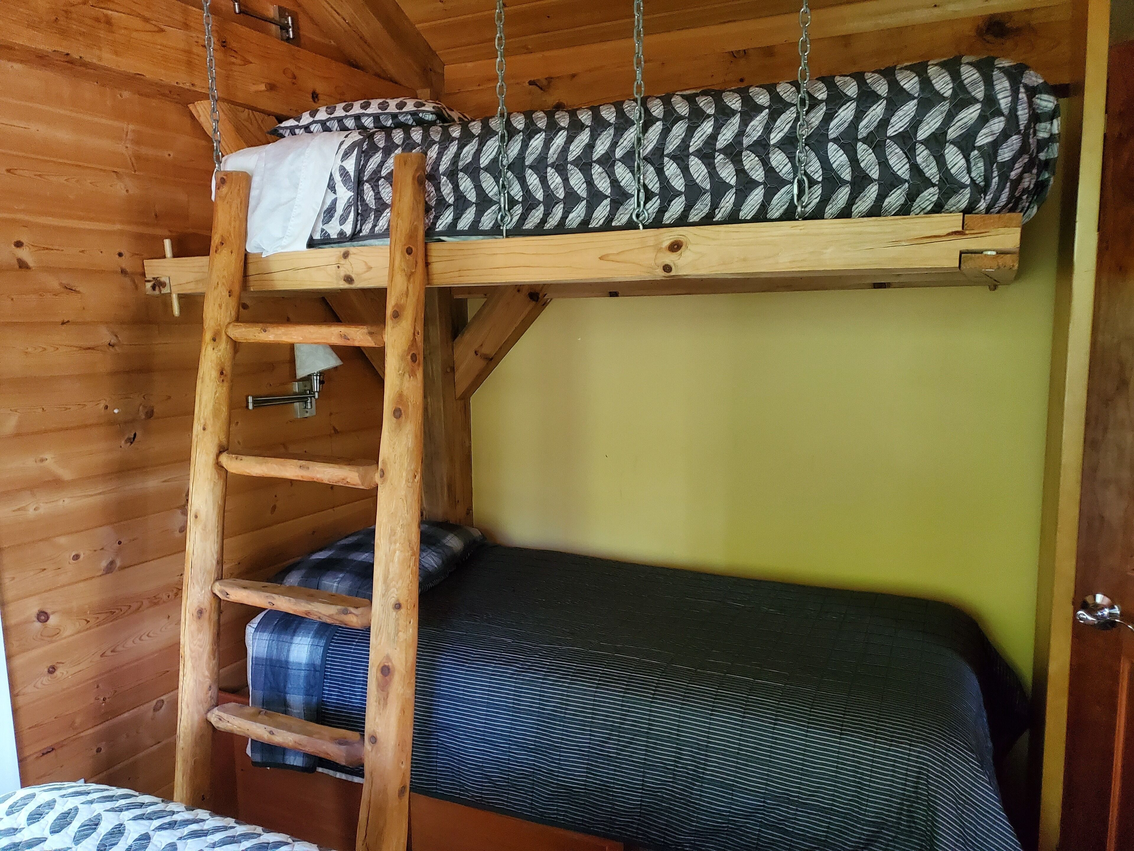 Ein Stockbett mit einer Leiter, ein Einzelbett darunter und eine Holzwand.