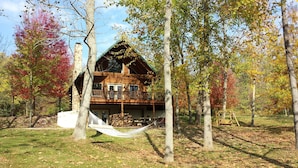 Uma cabana de toras com varanda, rodeada por árvores com folhagem outonal.
