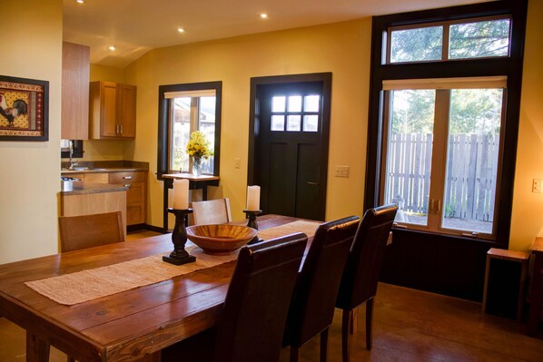 A dining area with a wooden table, chairs, a vase with flowers, and a door with windows.