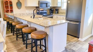 Cozinha com ilha central, banquetas, frigorífico e micro-ondas.