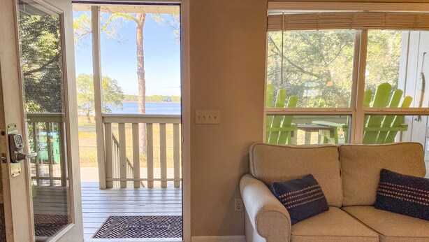 Quarto com sofá bege, porta que dá para um deck externo e vista para um lago.