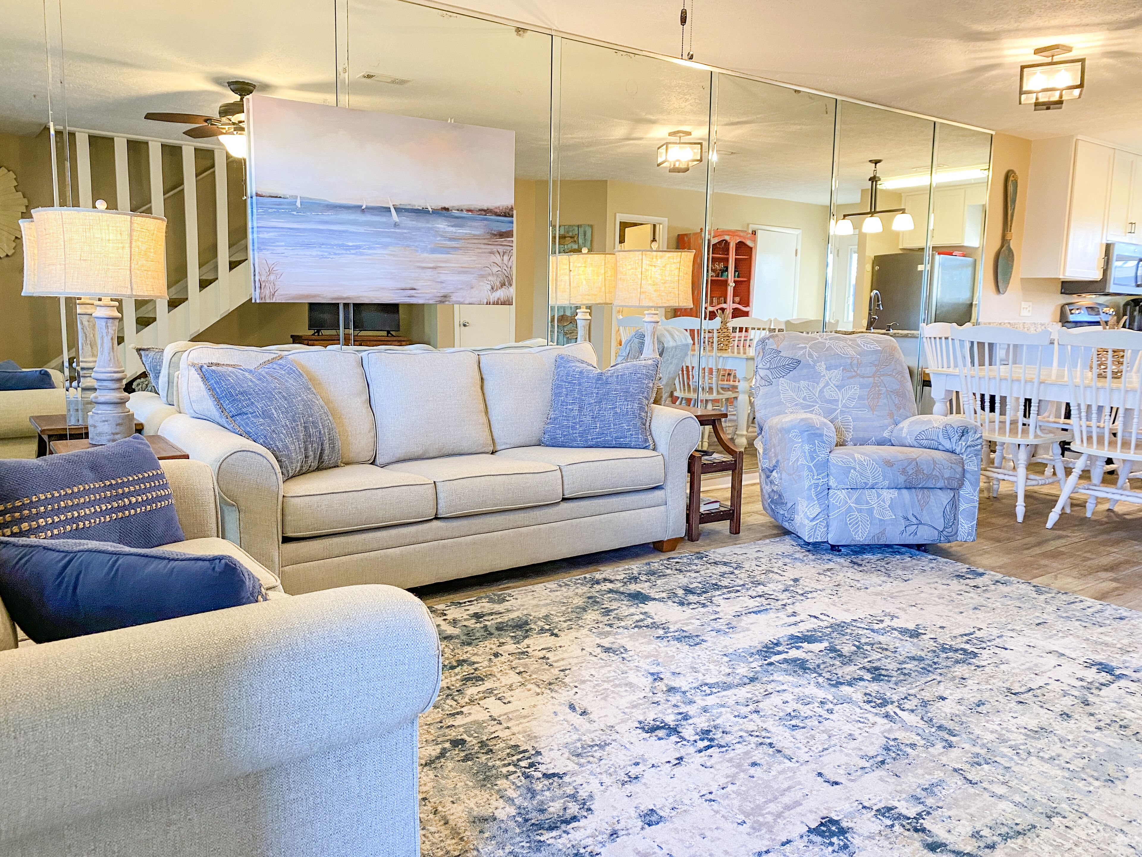 Una sala de estar con sofá, sillón y un cuadro grande de un paisaje marino.