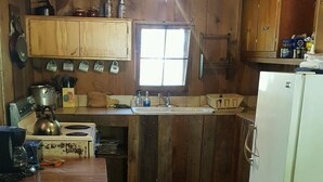 A rustic kitchen with wooden cabinets, a stove, a sink, and a refrigerator.