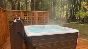 Un bain à remous sur une terrasse en bois, entouré d’une clôture en bois et d’arbres.