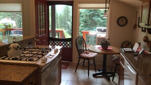 A kitchen with a gas stove, a dining table with chairs, and a view of the outdoors through a door.