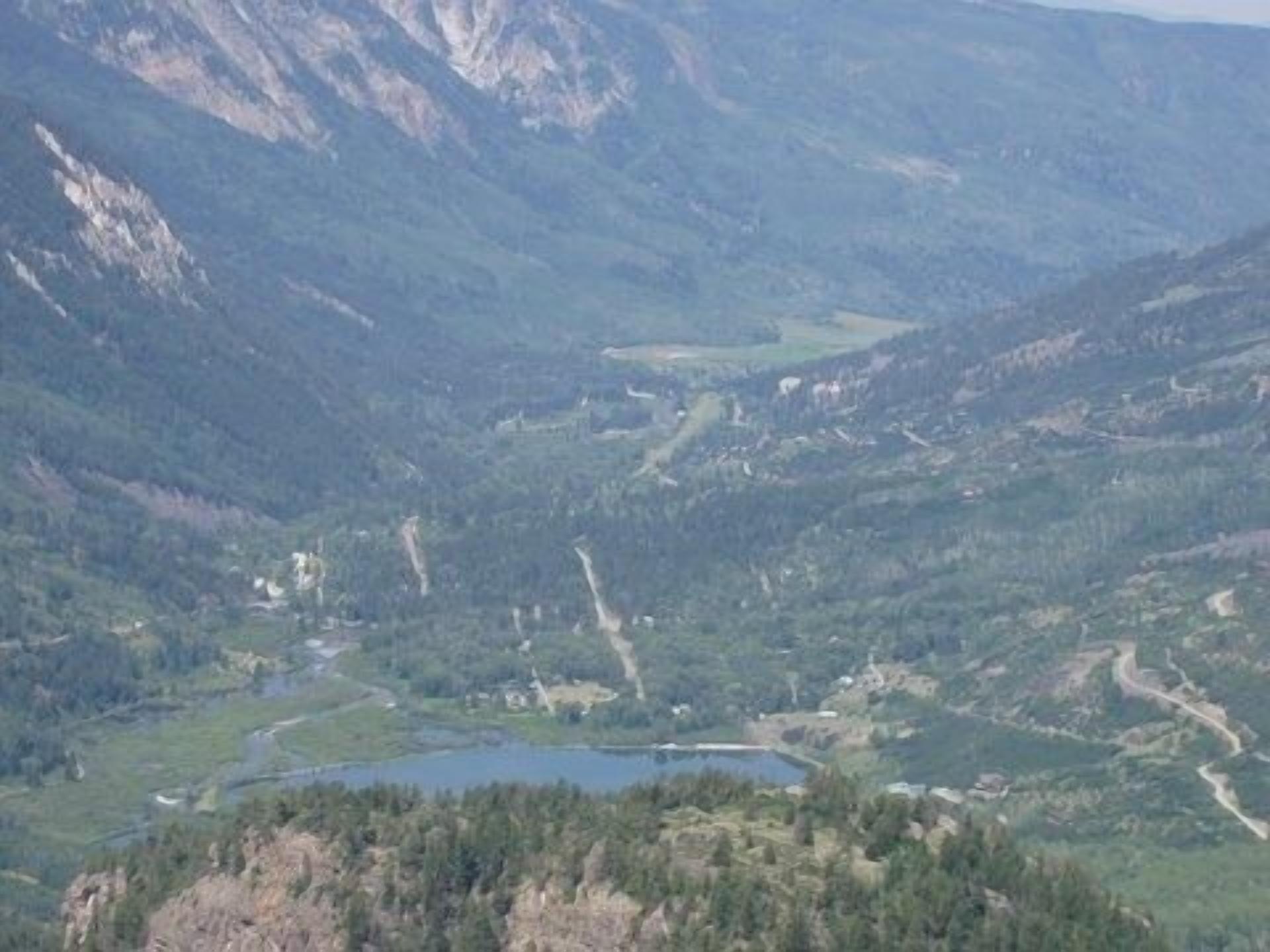 Un paisaje montañoso con un río, un lago pequeño y edificios dispersos.