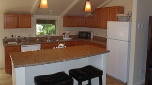 A kitchen with granite countertops, wooden cabinets, a white refrigerator, and two pendant lights.