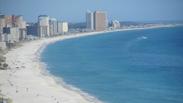 A beach with a long stretch of sand, a clear blue ocean, and several buildings in the background. - Beautiful Majestic Beach Towers Resort #2109  (Panama City Beach)