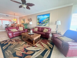 A living room with a ceiling fan, a large painting, and a dining area in the background.