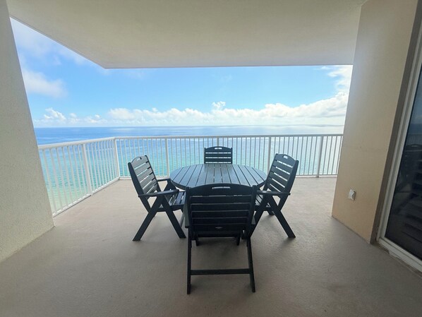 A balcony with a table and chairs, overlooking a clear blue sky and calm sea.