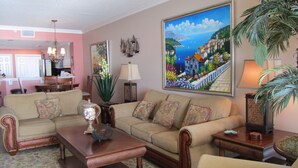 A living room with a sofa, a coffee table, and a painting of a coastal scene. - Beautiful Majestic Beach Towers Resort #2109  (Panama City Beach)