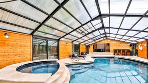 Una piscina interior con techo de cristal, paredes de madera y un área de descanso con sillones.