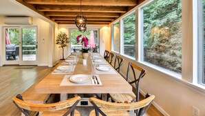 Una larga mesa de comedor con sillas, dispuesta para una comida, en una habitación con vigas de madera y ventanas amplias.
