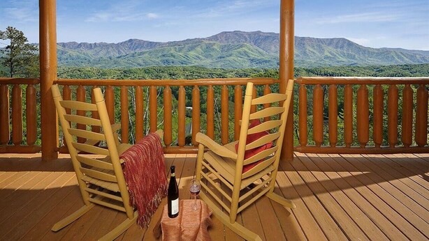 A wooden deck with two wooden chairs, a bottle of wine, and a glass on the table. - Broken Spoke is a great cabin with an awesome View (Sevierville)