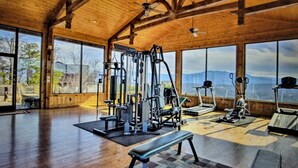 A spacious gym with various exercise equipment, large windows, and a wooden interior. - Broken Spoke is a great cabin with an awesome View (Sevierville)