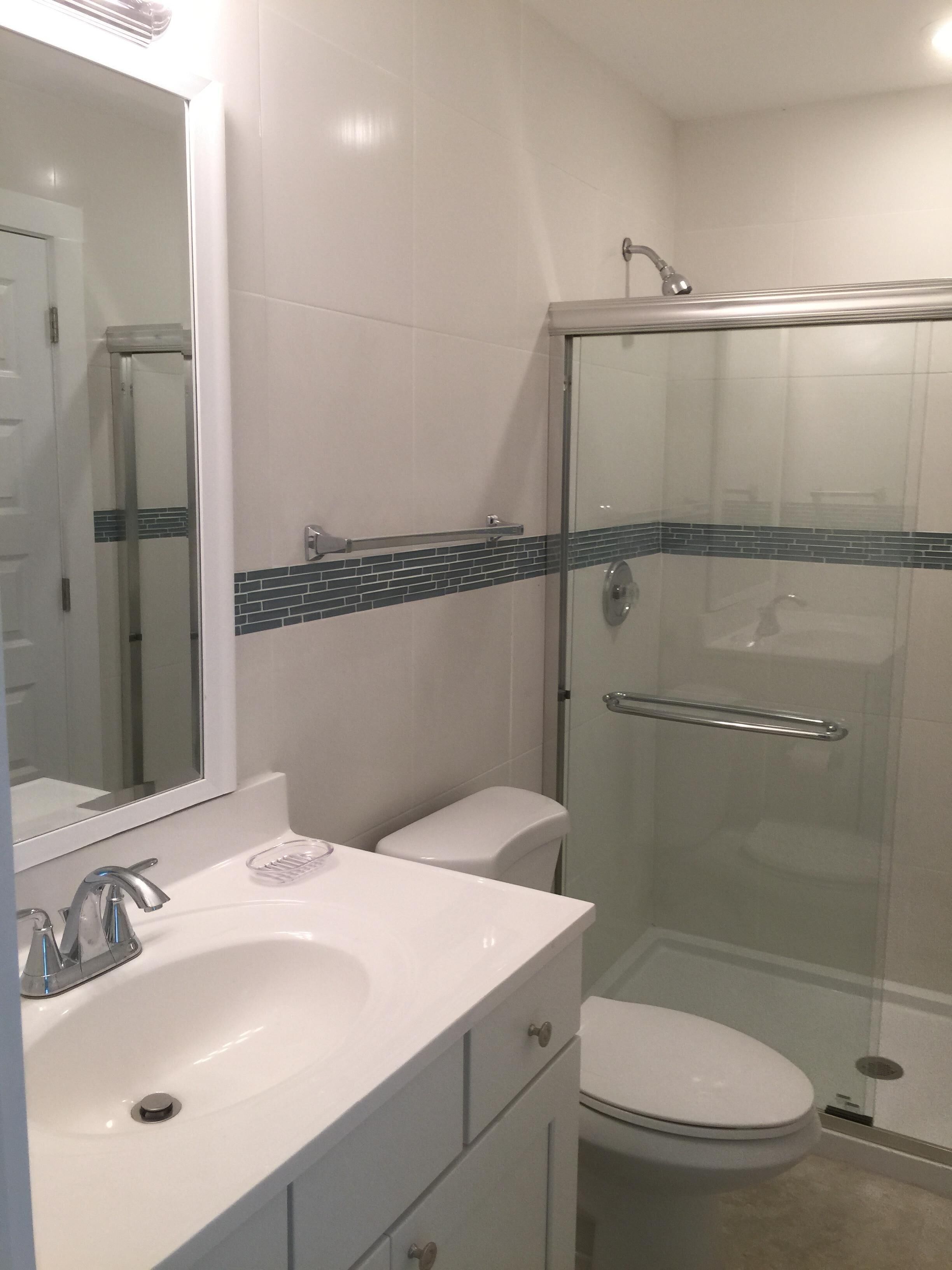 A bathroom with a white sink, mirror, and toilet. It includes a glass-enclosed shower area with a glass door and a metal showerhead.