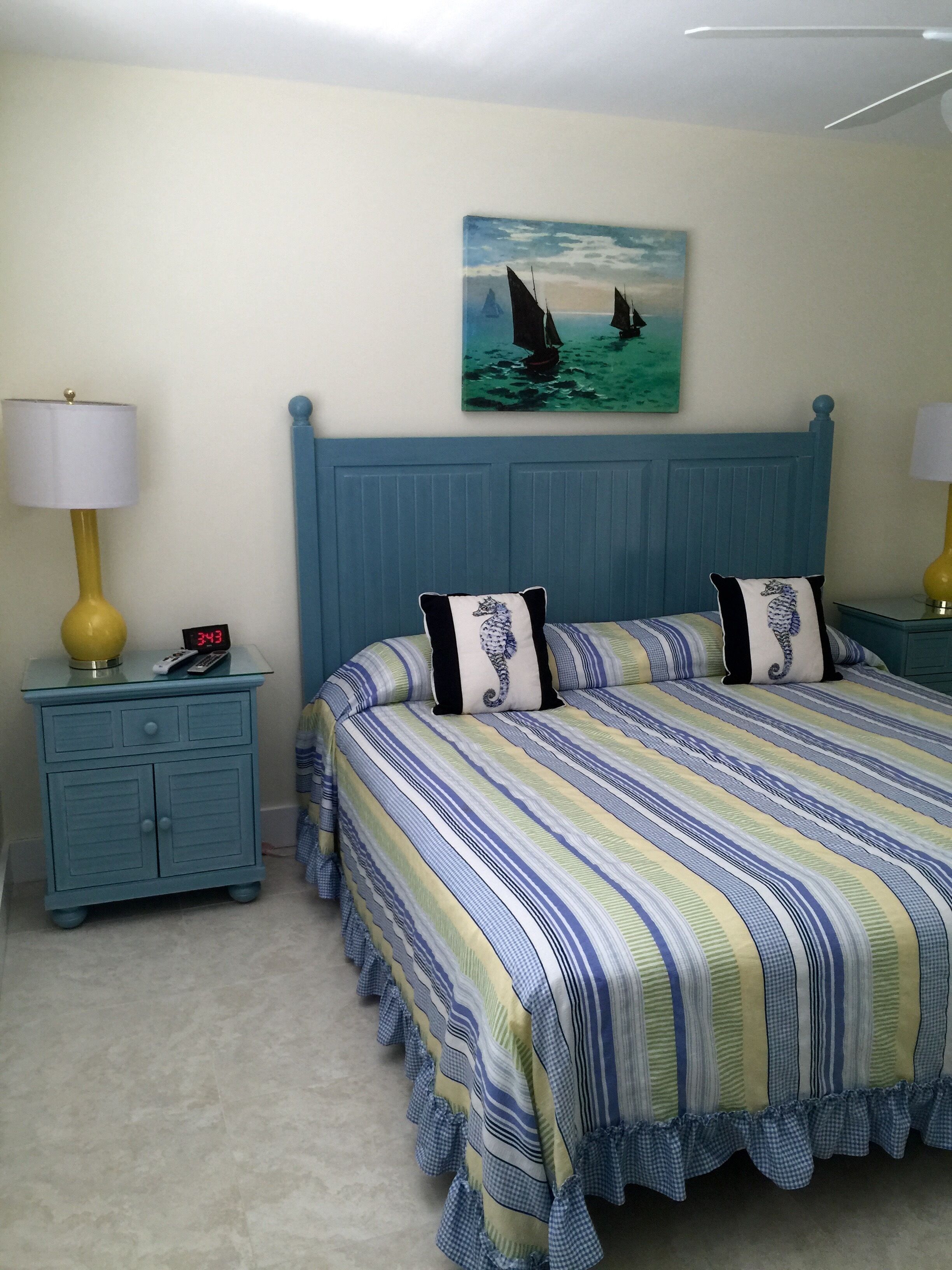 A bedroom with a bed, two nightstands, a painting, and a clock.