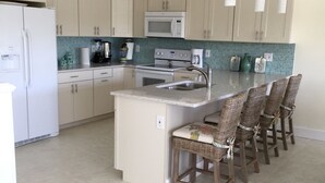 Una cucina con mobili bianchi, un'isola centrale con sgabelli da bar, un forno a microonde e un piano cottura.