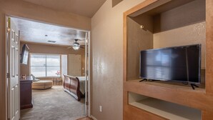 Une pièce comprenant un téléviseur posé sur un meuble en bois, un lit avec une tête de lit, un bureau et une chaise.