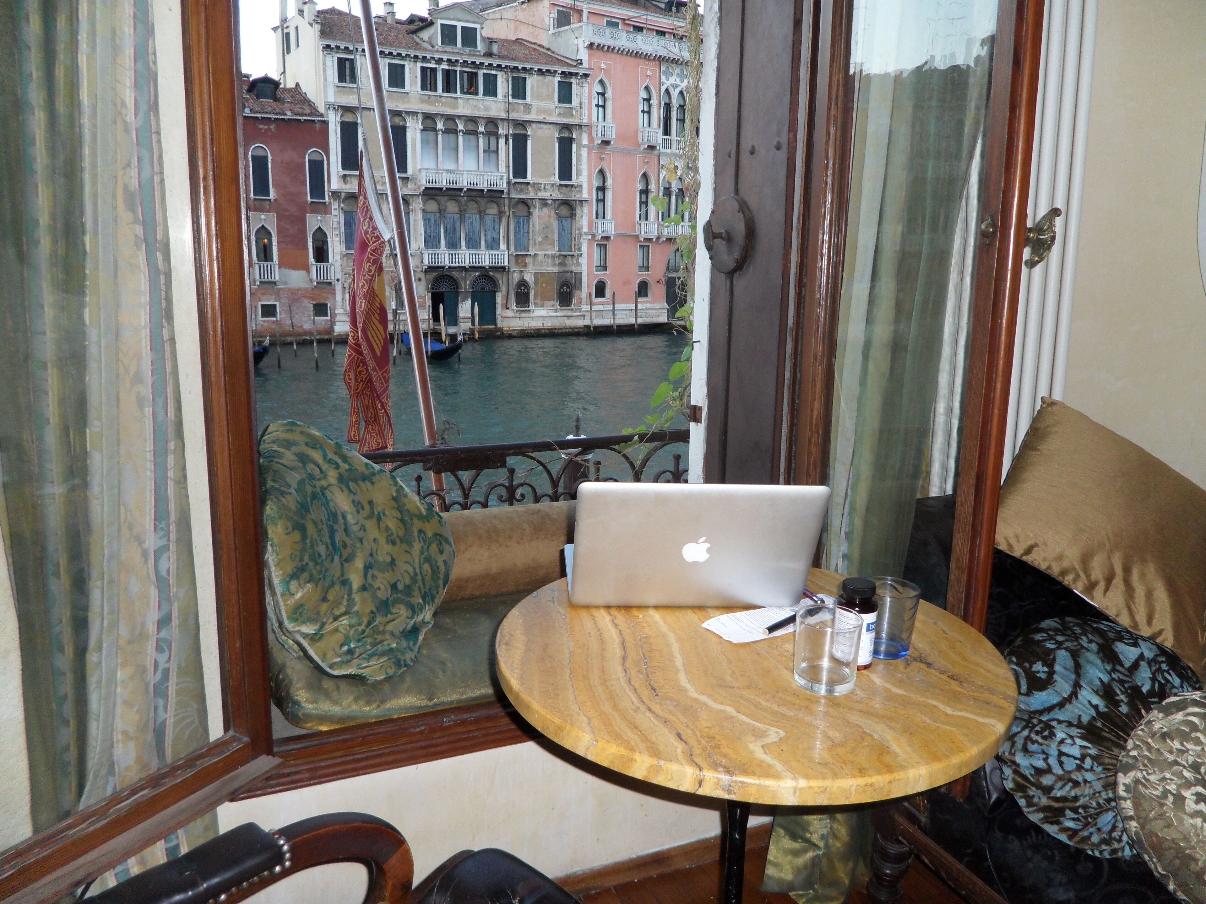 A room with a view of Venice's canals, a laptop on a small round table, and a sofa with patterned cushions.