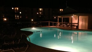 A swimming pool at night with lounge chairs and a covered area.