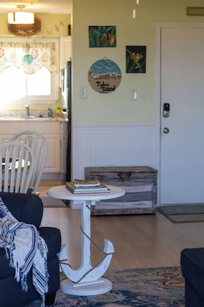 A living room with a round table, a white chair, a sofa, a rug, and a door in the background.
