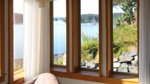 A room with large windows overlooking a lake, wooden beams on the ceiling, and a bed with a white headboard. - Beachside Retreat-Oceanfront Home (Kodiak)