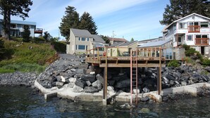 A waterfront property with a wooden deck, a stone retaining wall, and a house with a balcony. - Beachside Retreat-Oceanfront Home (Kodiak)