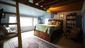 A bedroom with a wooden bed, a bookshelf, a chair, and a window. - Beachside Retreat-Oceanfront Home (Kodiak)