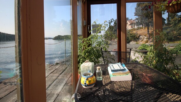 A table with a book, a jar, and a decorative item on a deck overlooking a lake. - Beachside Retreat-Oceanfront Home (Kodiak)