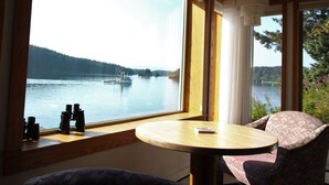 A room with a large window overlooking a lake, a small round table, and a chair. - Beachside Retreat-Oceanfront Home (Kodiak)