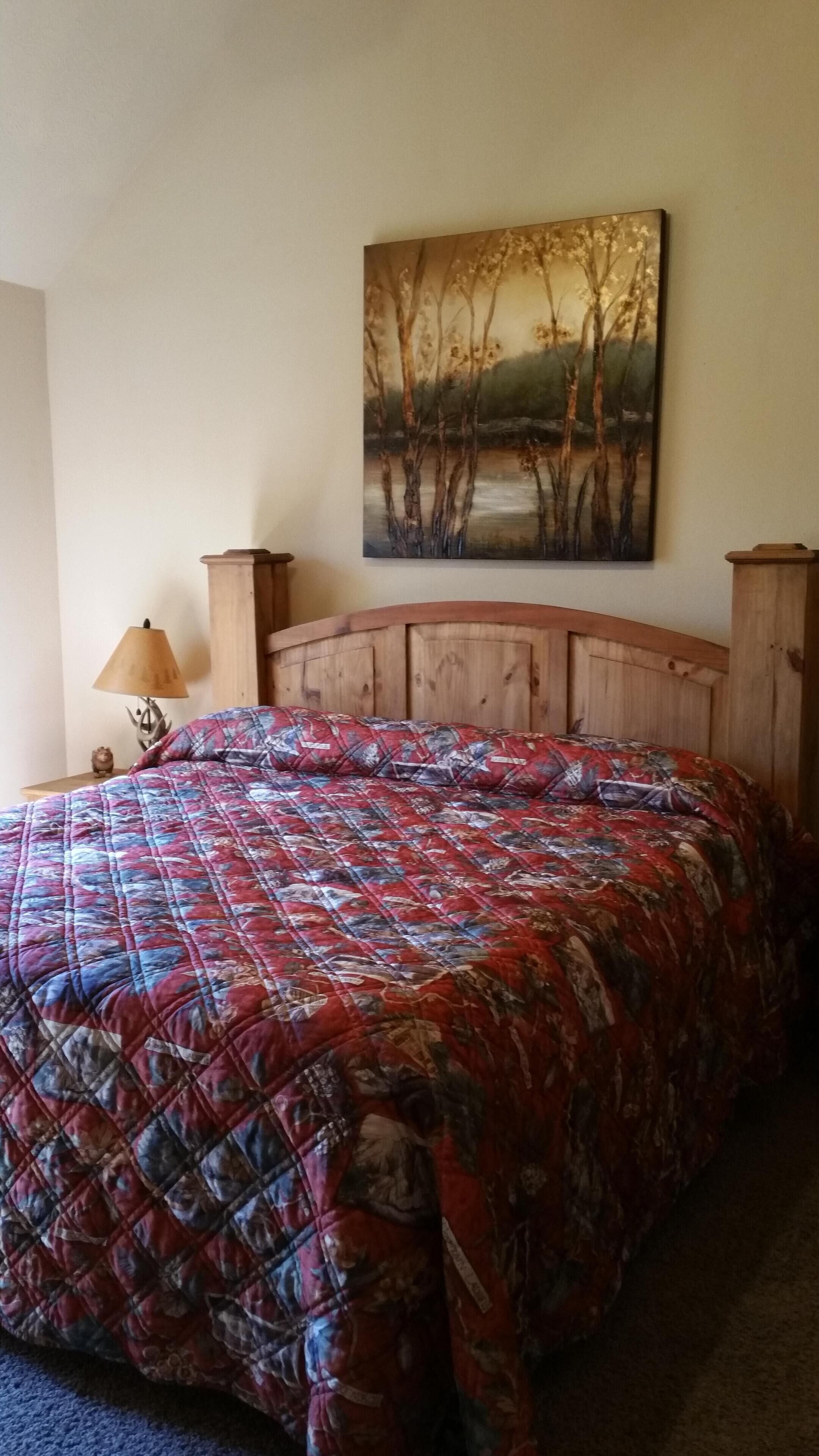 Une chambre à coucher avec une tête de lit en bois, une couvre-lit à motifs floraux, un tableau représentant des arbres et une lampe sur une table de chevet.