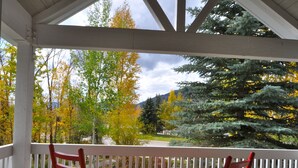 A covered porch with two red rocking chairs and a white railing, overlooking a landscape with autumn-colored trees and a mountain in the distance. - Exclusive Teton Pines Home off Teton Village Rd. 5 min from Teton Village Skiing (Wilson)