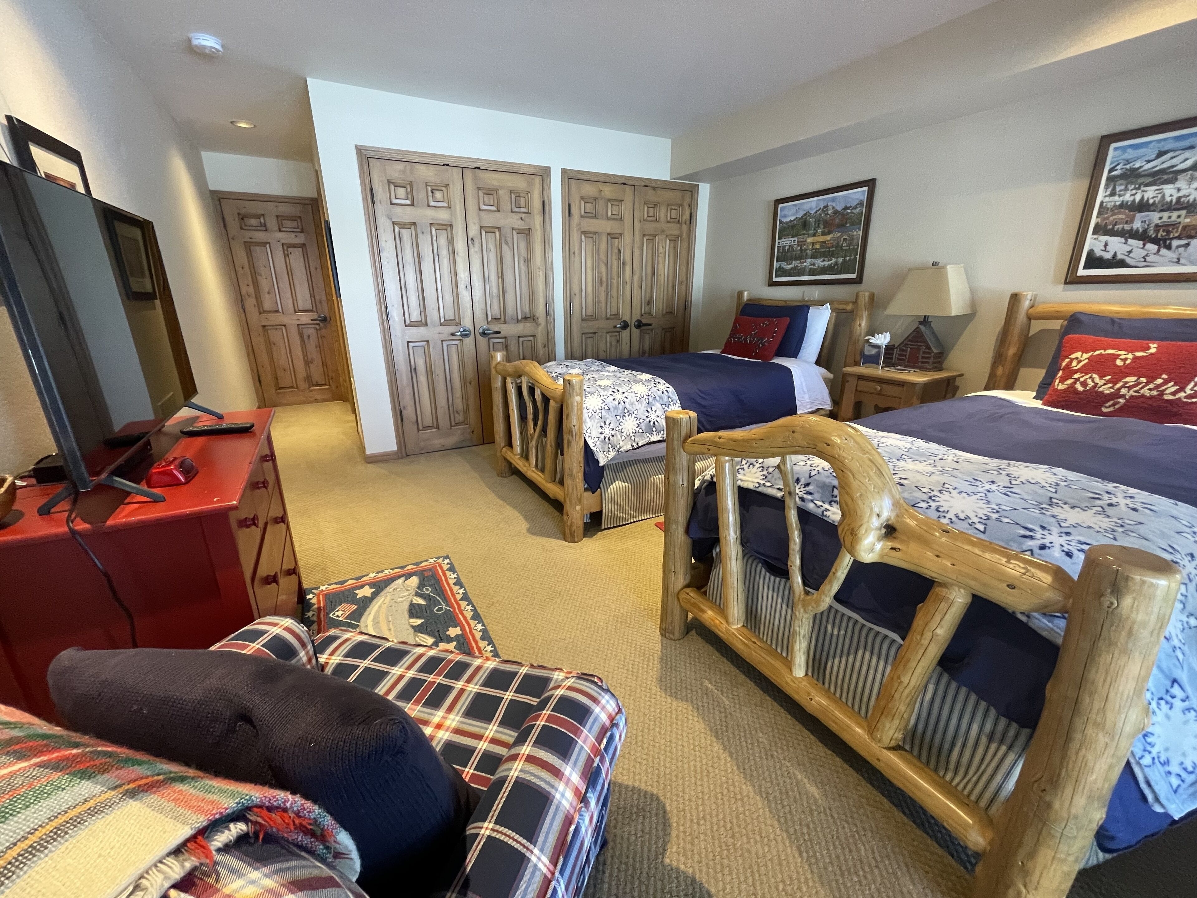 A hotel room with two beds, a wooden headboard, a red desk, a mirror, and a large window.