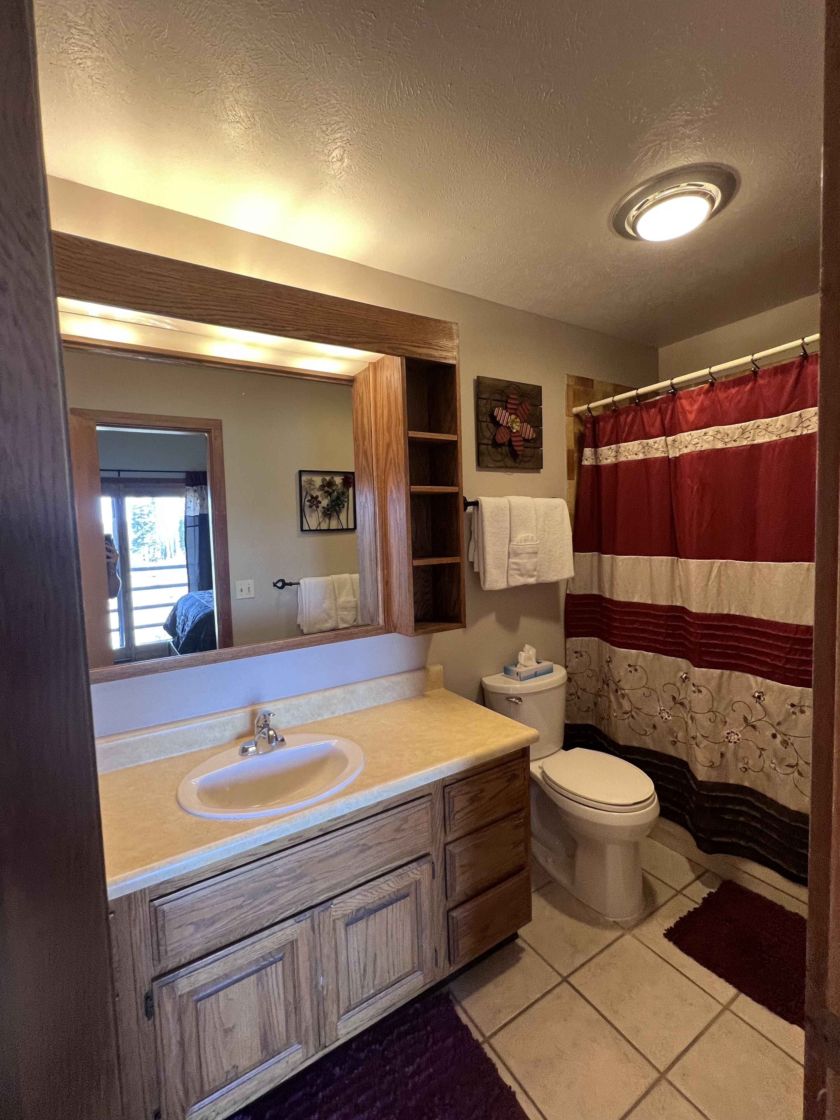 Une salle de bain avec un meuble-lavabo en bois, un évier, des toilettes et un rideau de douche.