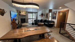 A modern living room with a large wooden dining table, a black leather sofa, and a fireplace. - walking distance to skiing and nightlife in Northstar resort (Truckee)