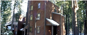 A multi-story wooden building with multiple windows and a covered entrance, surrounded by tall trees. - walking distance to skiing and nightlife in Northstar resort (Truckee)