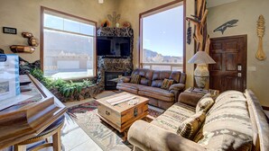 A spacious living room with a piano, a large window, a fireplace, and a cozy seating area. - High End Southwest Luxury, Spa-like Baths, Steam Shr, Sauna, Garage,Pool,Hot Tub (Moab)