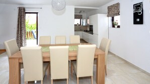 Ein Essbereich mit einem Holztisch und sechs Stühlen, im Hintergrund eine Küche und ein Balkon mit Blick.