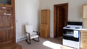 A kitchen with a stove, a wooden cabinet, a rocking chair, and a door with an exit sign.